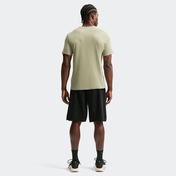 Back view of a man wearing a light olive green Nike Men's Dri-Fit Training T-Shirt and black athletic shorts on a plain