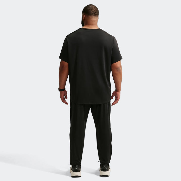 Rear view of a man wearing a black short-sleeve t-shirt and Nike Miler Black Men's Dri-Fit Knit Running Pants, with sneakers.
