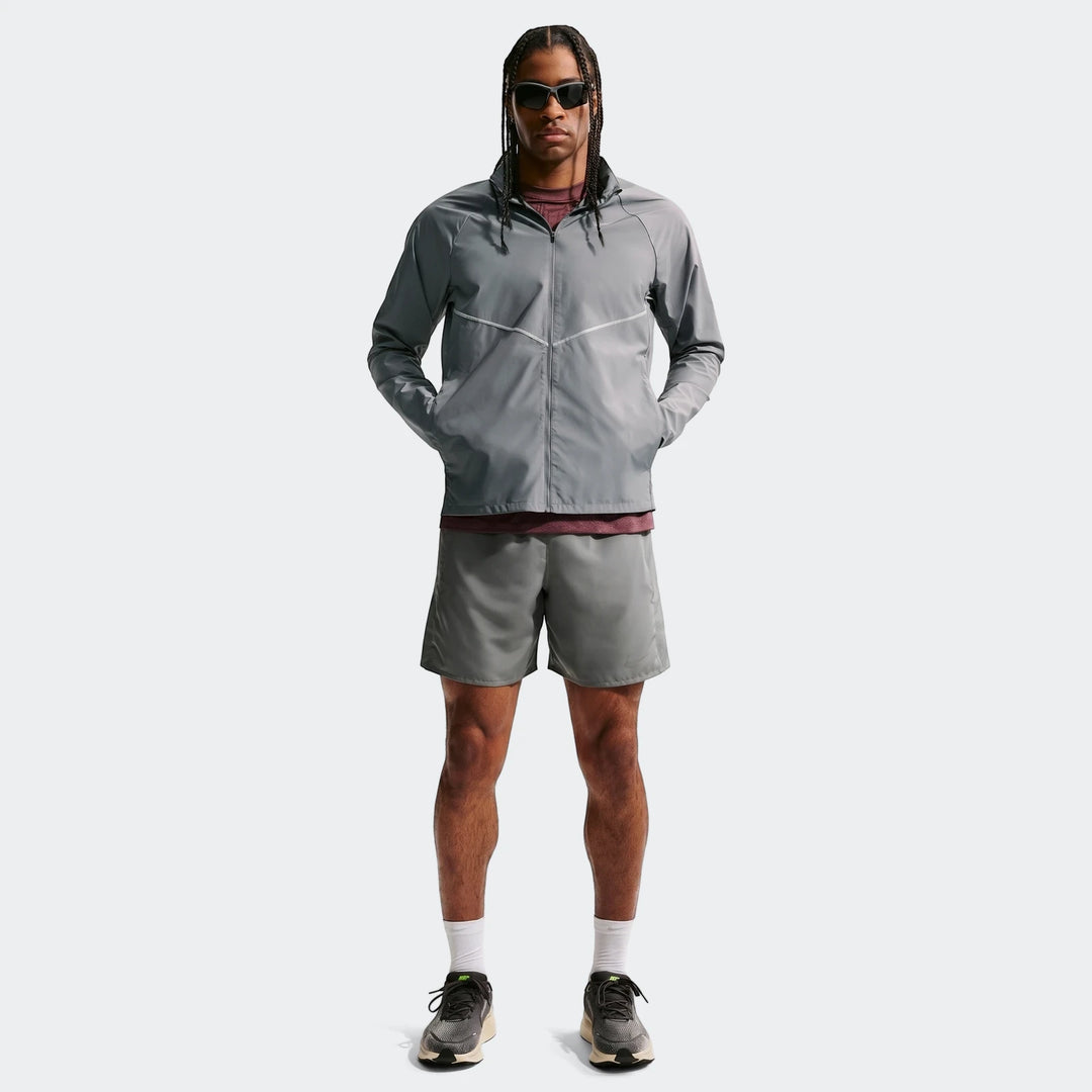 Full-body shot of a male model wearing a grey Nike Miler Repel UV Protection Running Jacket, grey shorts, and athletic shoes.