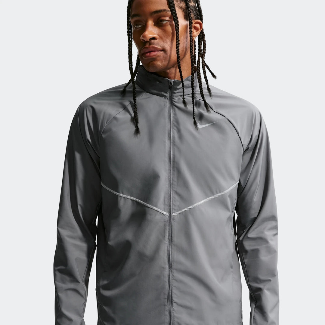 Grey Nike Miler men's running jacket featuring UV protection, worn by a man with braided hair. Front view, studio shot.