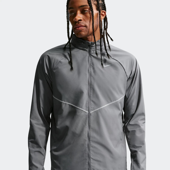 Grey Nike Miler men's running jacket featuring UV protection, worn by a man with braided hair. Front view, studio shot.