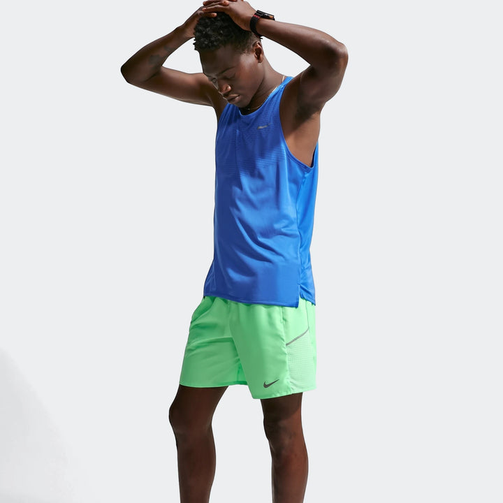 Man wearing vibrant green Nike Miler Dri-Fit 7" Brief-Lined Running Shorts and a blue athletic tank top, hands on head.