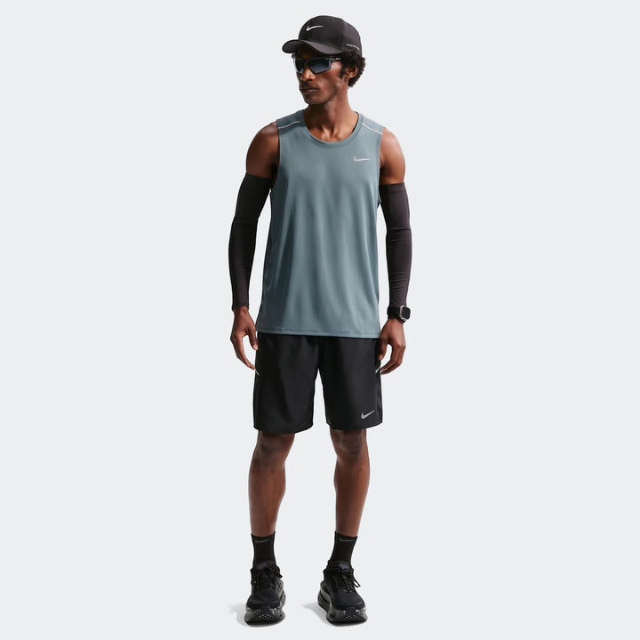 Full body shot of a man in Nike Miler Men's Dri-Fit 9" Unlined Running Shorts, blue tank top, and black cap, ready for a run.