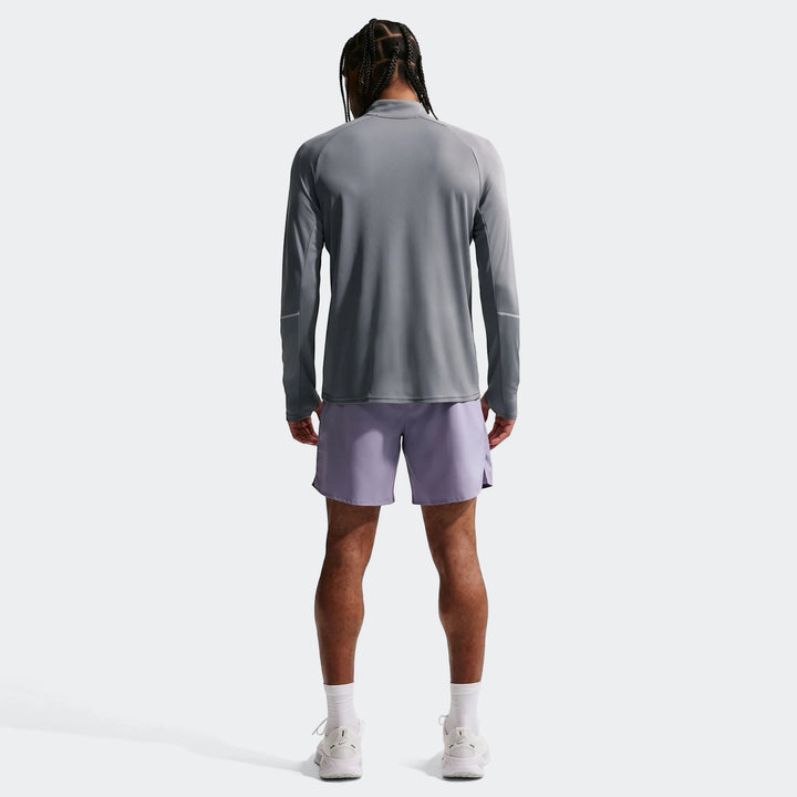Rear view of a man wearing a Nike Miler grey Dri-Fit 1/2-Zip Running Top and purple athletic shorts.