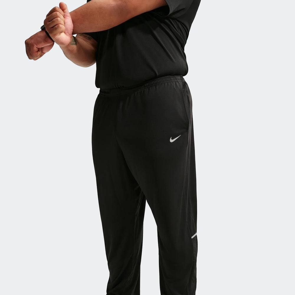 A person wearing Nike Miler men's Dri-Fit knit running pants in black, stretching their arm across their chest.