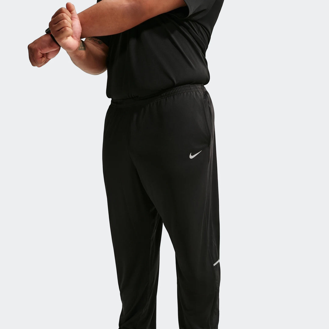 A person wearing Nike Miler men's Dri-Fit knit running pants in black, stretching their arm across their chest.