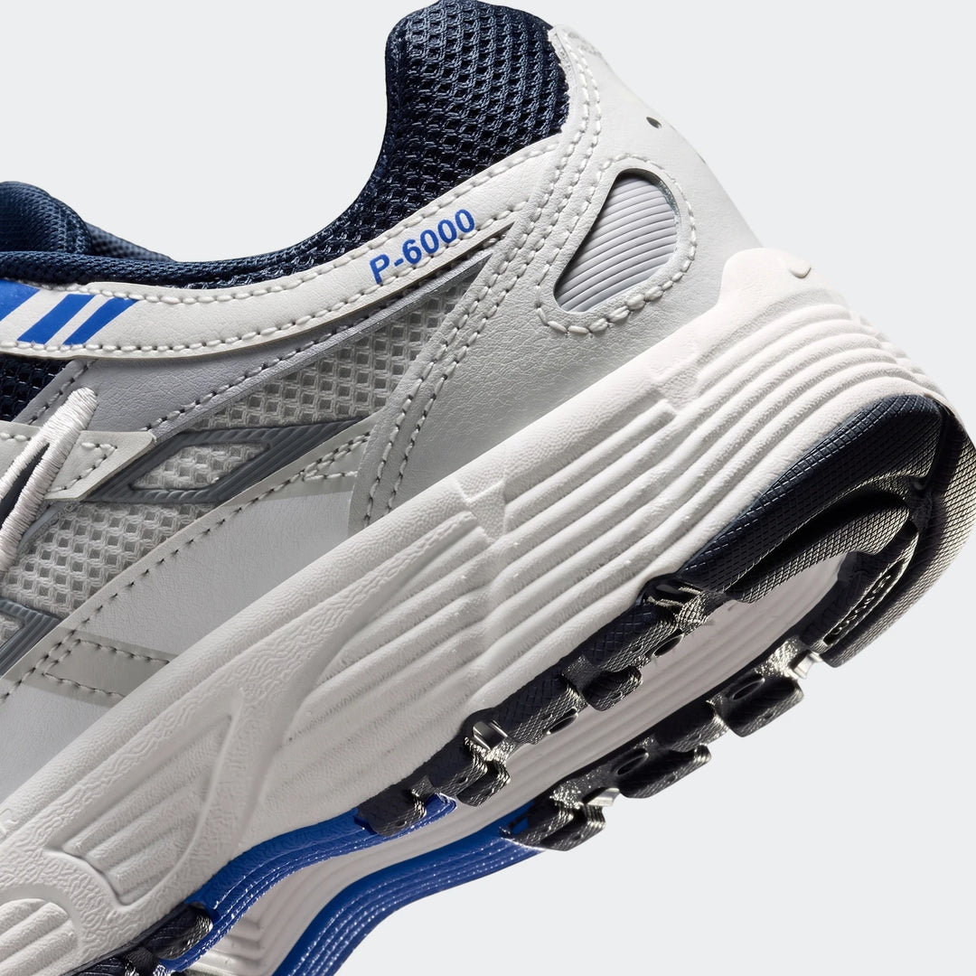 Close-up of a white, blue, and gray Nike P-6000 Big Kids' shoe, showing the side and heel with visible branding.