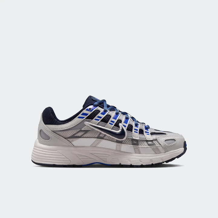 Nike P-6000 Big Kids' Shoes in light grey, white, navy blue, and royal blue, shown from a side view.