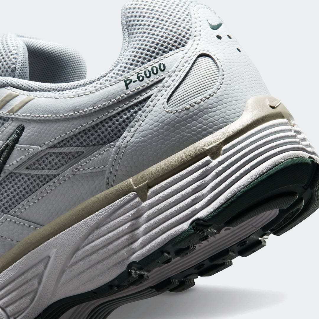 Angled close-up view of a Nike P-6000 men's athletic shoe in light grey with dark green and khaki accents, showcasing the
