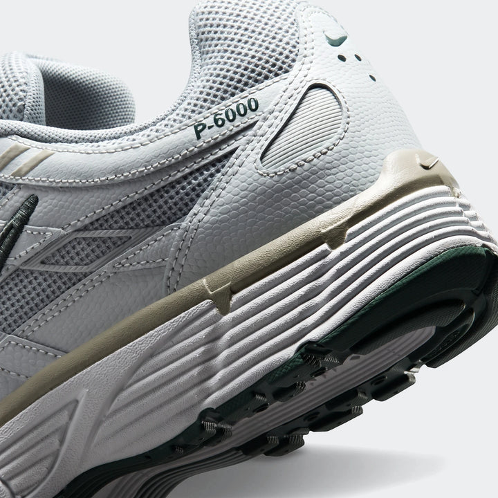 Angled close-up view of a Nike P-6000 men's athletic shoe in light grey with dark green and khaki accents, showcasing the
