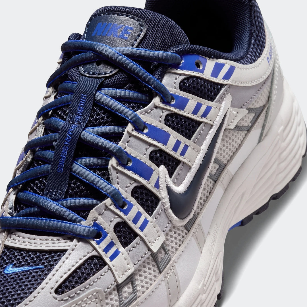 Close-up of Nike P-6000 Big Kids' Shoes in gray, blue, and white mesh and leather, featuring blue laces.