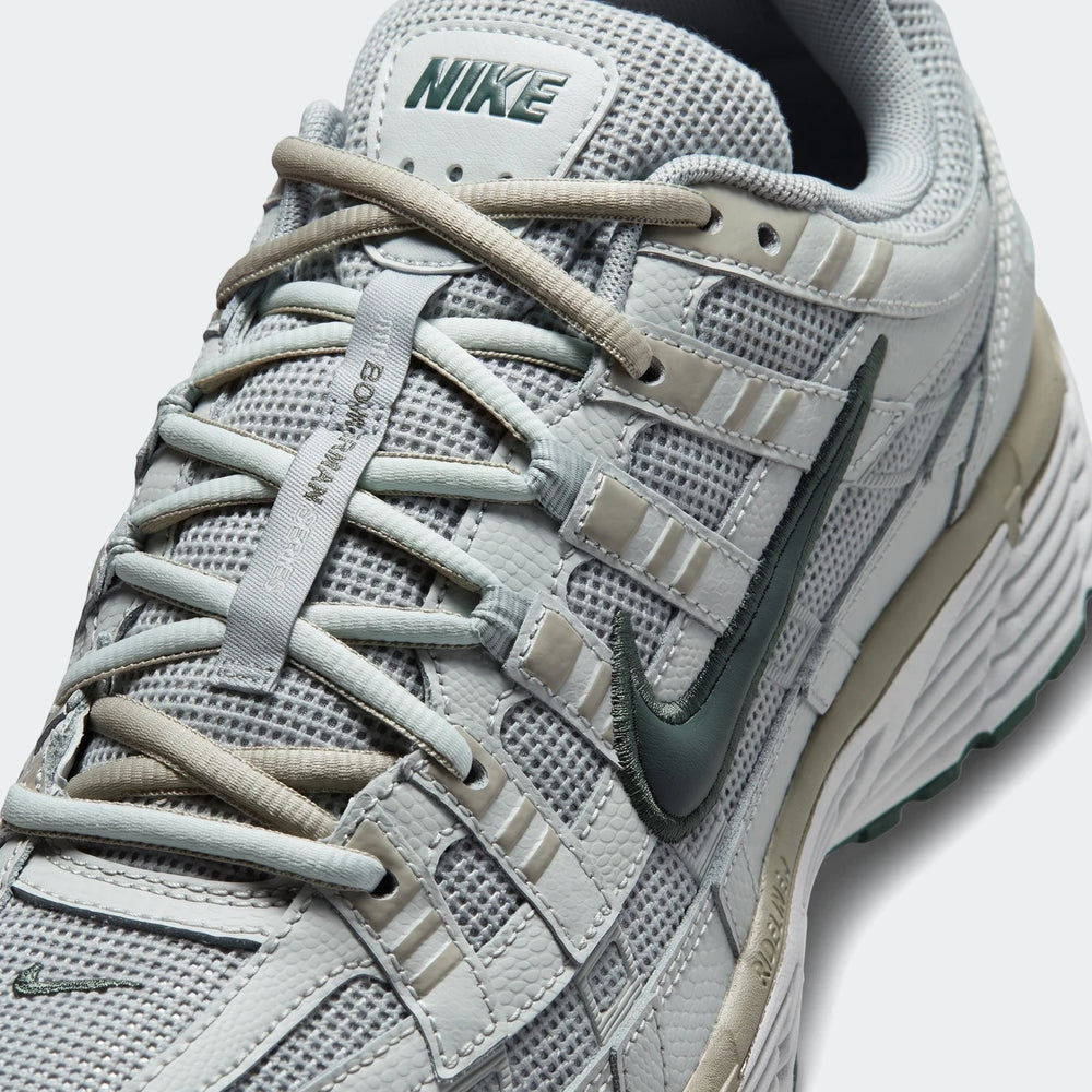 Close-up of a gray and green Nike P-6000 men's athletic sneaker, showcasing the intricate mesh, leather overlays, and iconic