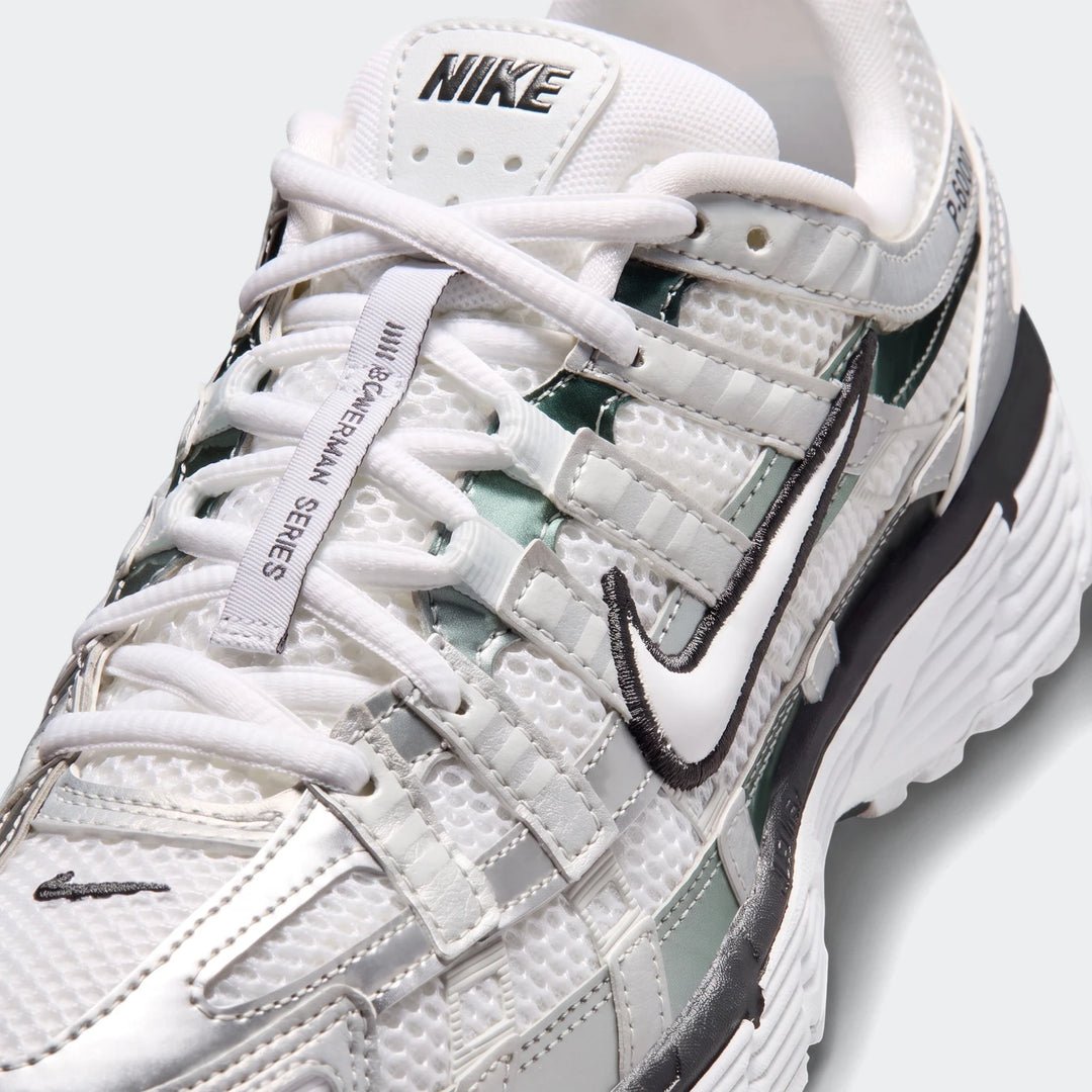 Close-up of Nike P-6000 women's shoes in white and silver mesh with dark green accents, showing the side profile and laces.