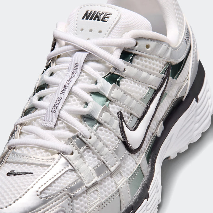 Close-up of Nike P-6000 women's shoes in white and silver mesh with dark green accents, showing the side profile and laces.