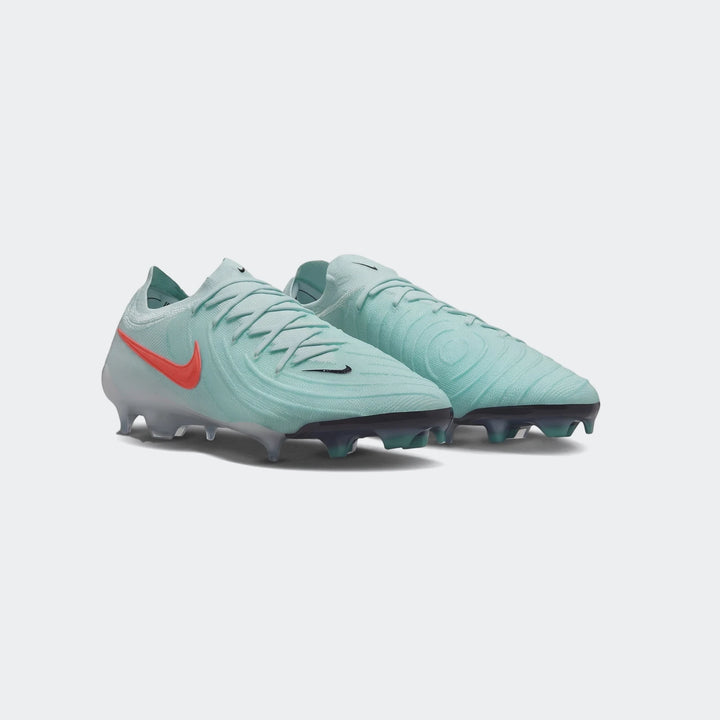 A pair of Nike Phantom Gx 11 Club Fg/Mg Green Boots in teal/mint green with an orange swoosh and black studded soles, ready