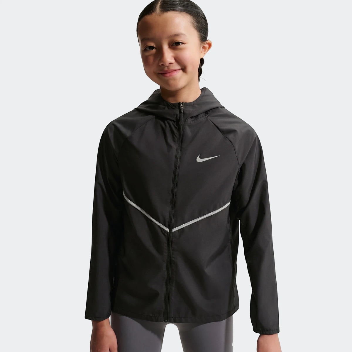 Young girl wearing a black Nike+ Repl Miler Jacket with a silver swoosh logo and reflective stripes, featuring a full zipper