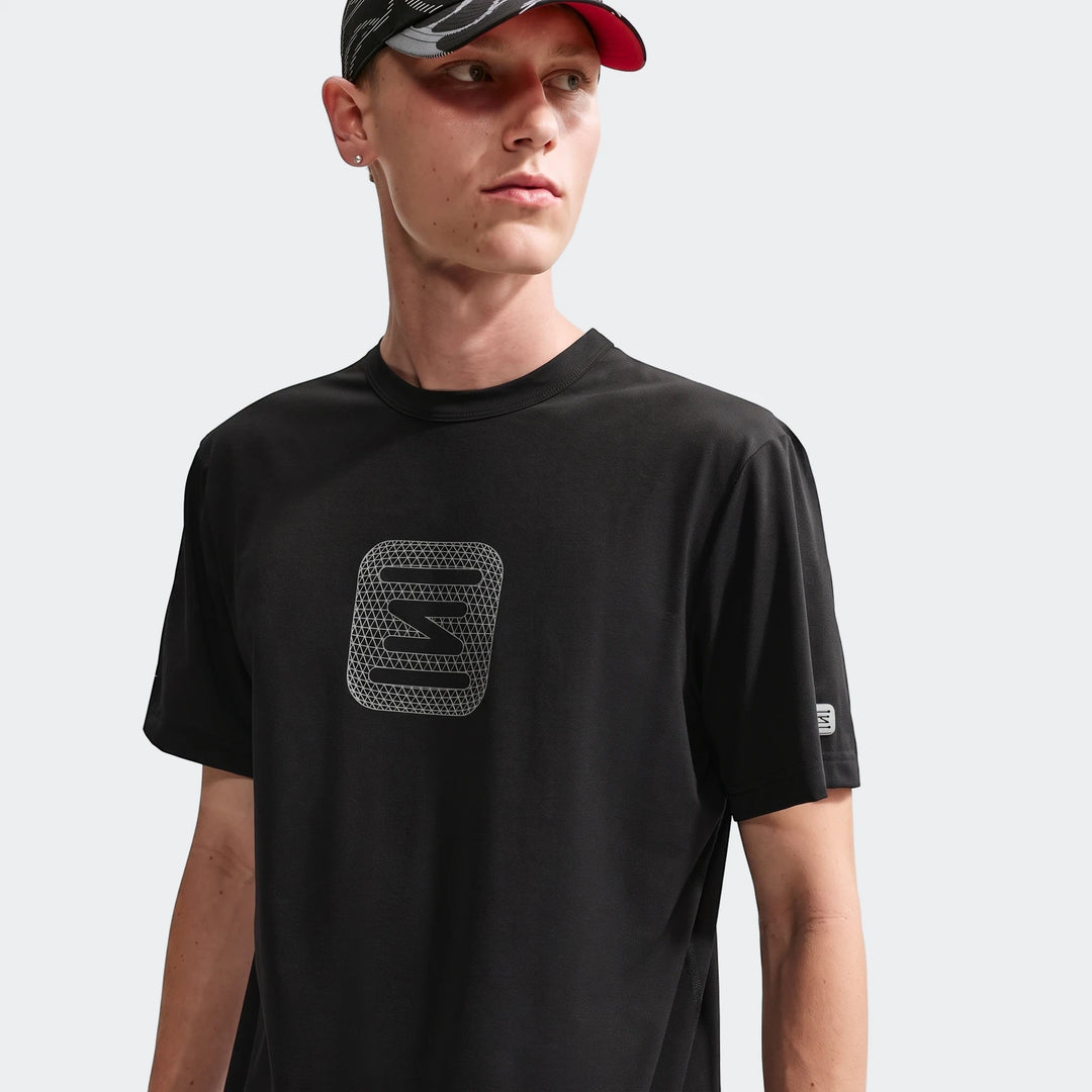 Nike Shox T-Shirt Mens Core Black with a white geometric logo, worn by a male model with a patterned cap, looking right.