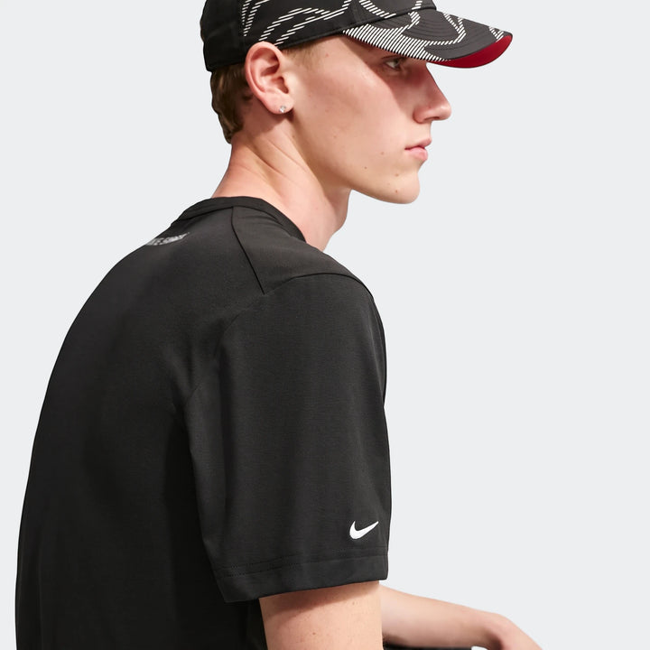 Close-up profile of a man wearing a black Nike Shox T-Shirt with white swoosh logo and a patterned cap.