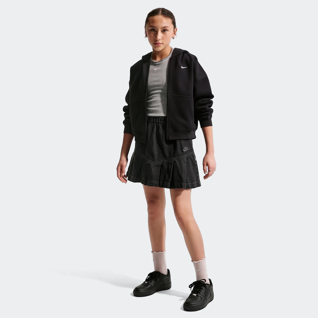 Young girl models a black Nike Sportswear Big Kids' denim pleated skirt, black hoodie, and grey t-shirt with black Nike