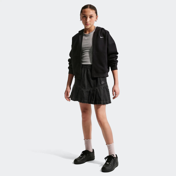 Young girl models a black Nike Sportswear Big Kids' denim pleated skirt, black hoodie, and grey t-shirt with black Nike
