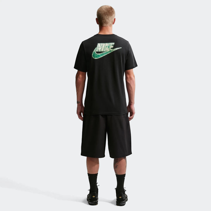 Rear view of a male model wearing a black Nike Sportswear t-shirt featuring a green distressed logo, paired with black
