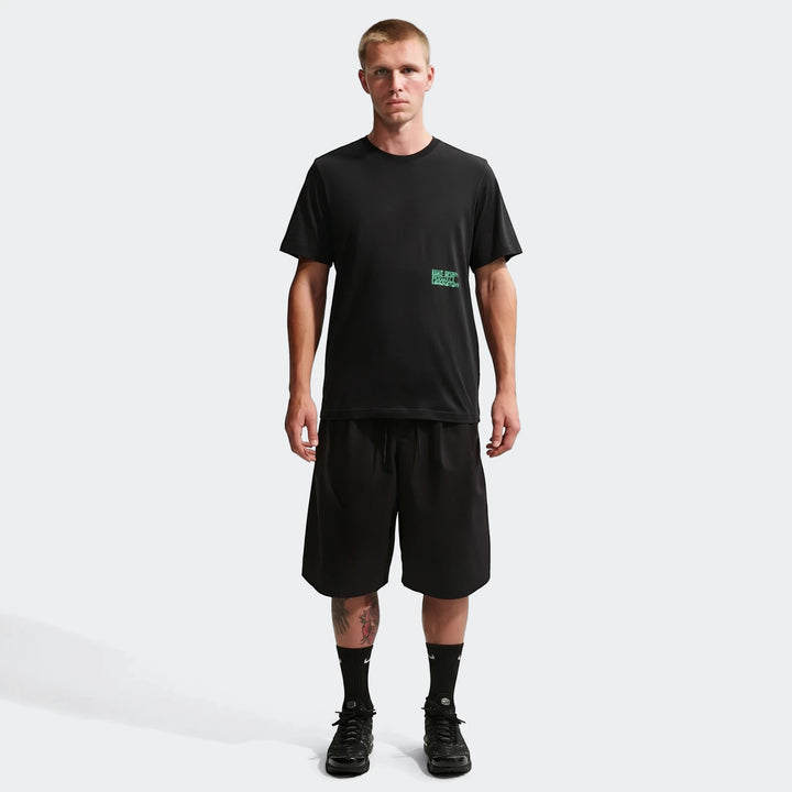 A male model wears a Nike Sportswear black t-shirt with a green graphic, black shorts, and black sneakers.