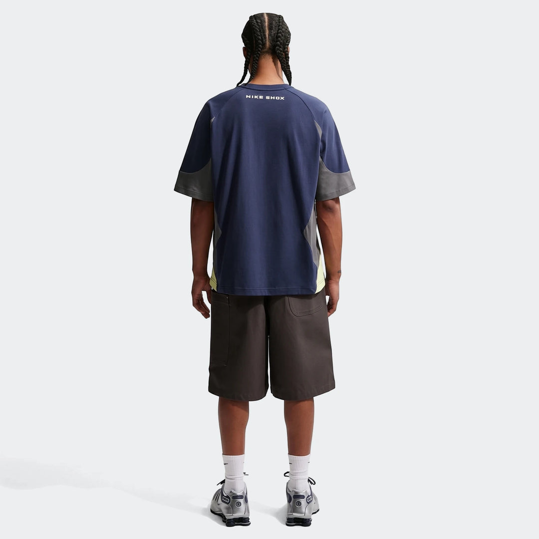 Back view of a man wearing a Nike Sportswear blue, grey, and neon yellow color-blocked short-sleeve top, dark grey shorts,