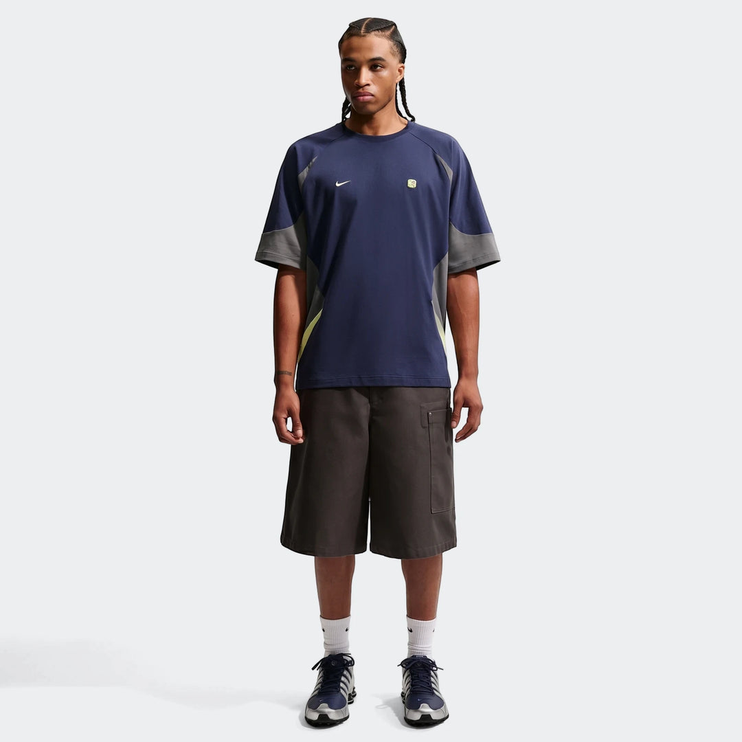 Full body image of a man modeling a Nike Sportswear blue men's short-sleeve top with gray and lime green accents, paired