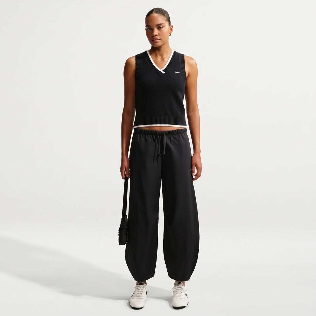 A female model wearing a black Nike Sportswear Chill Knit Women's Loose Sweater Vest, black drawstring pants, and white