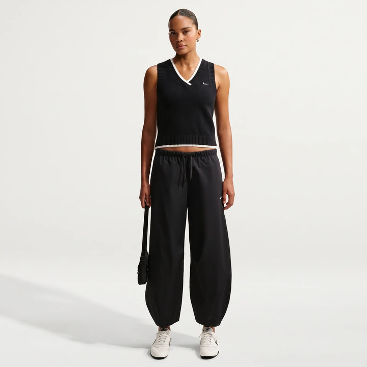 A female model wearing a black Nike Sportswear Chill Knit Women's Loose Sweater Vest, black drawstring pants, and white