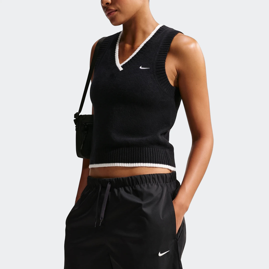 Model wearing a black Nike Sportswear Chill Knit Women's Loose Sweater Vest with white trim, paired with black track pants.