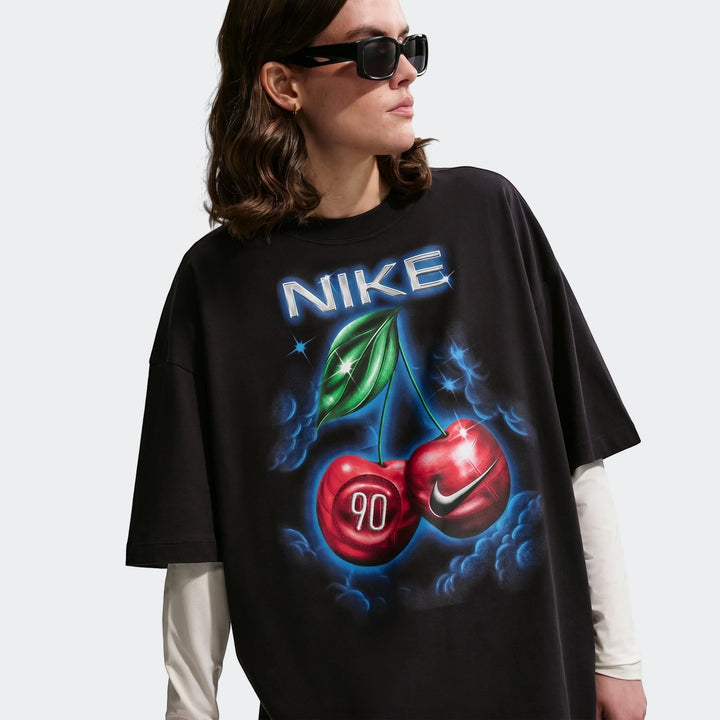 Nike Sportswear Classic black oversized t-shirt for women, featuring a vibrant cherry and Nike logo graphic, worn by a model.