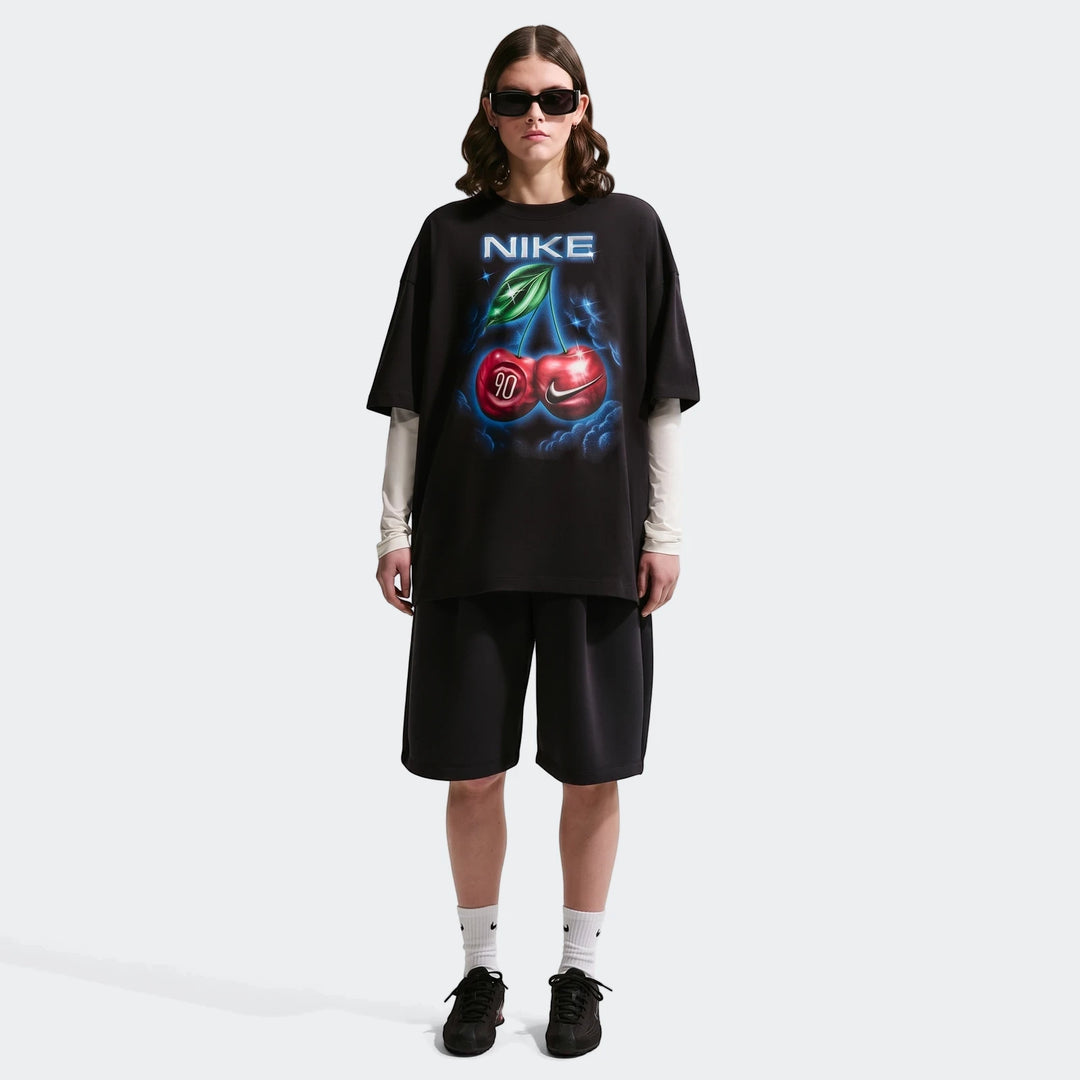 Nike Sportswear Classic Black Women's Oversized T-Shirt with a cherry graphic, worn by a model in black shorts and sneakers.