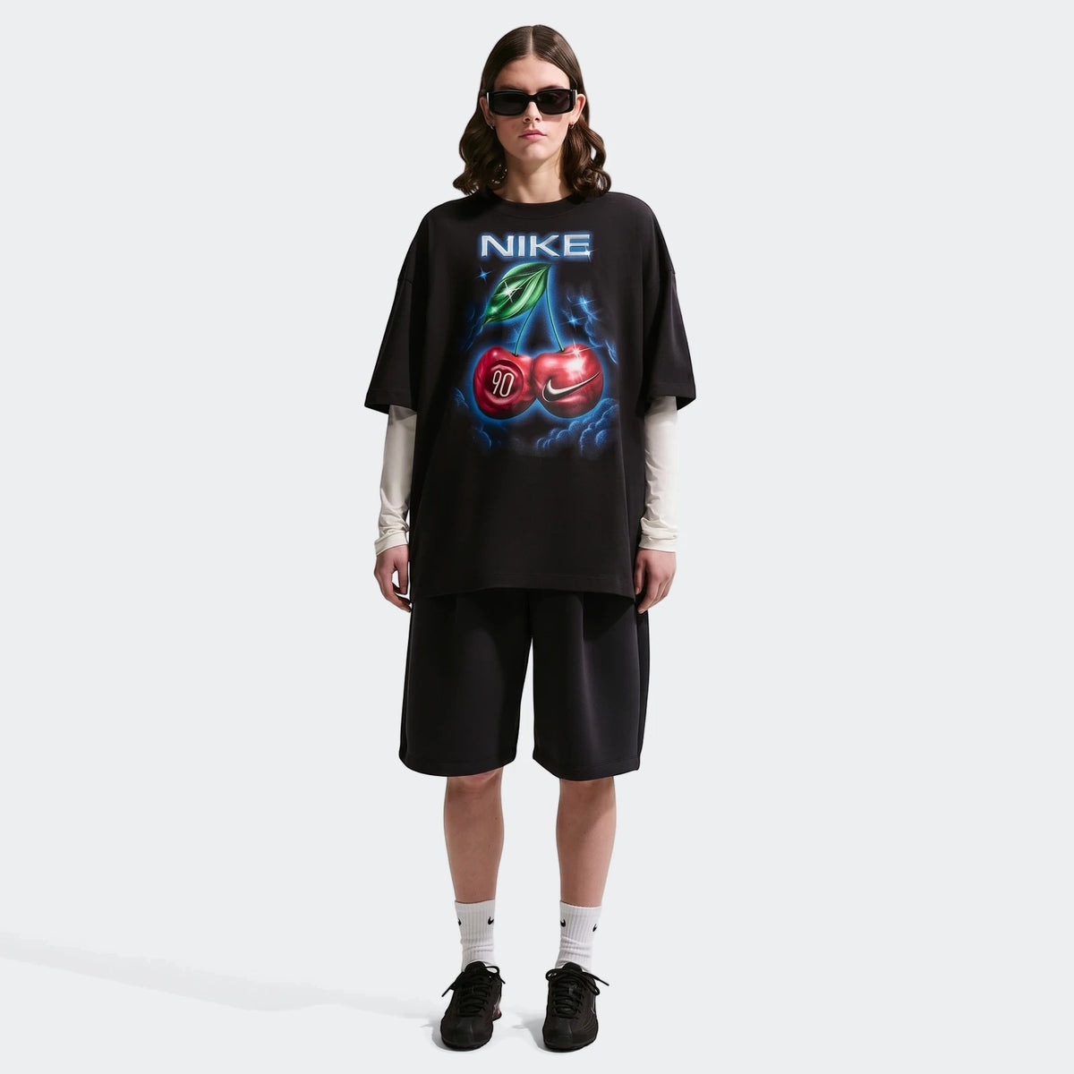 Nike Sportswear Classic Black Women's Oversized T-Shirt with a cherry graphic, worn by a model in black shorts and sneakers.