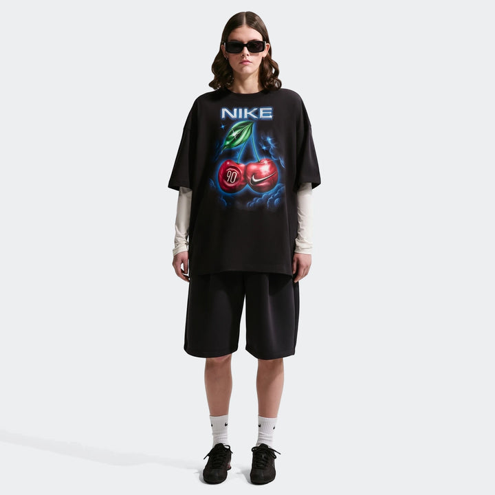Nike Sportswear Classic Black Women's Oversized T-Shirt with a cherry graphic, worn by a model in black shorts and sneakers.