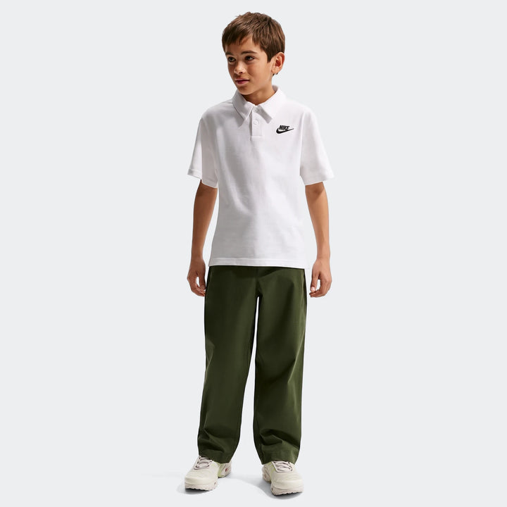 Nike Sportswear Club Big Kids' Knit Short-Sleeve Polo in white worn by a boy, paired with olive green pants, standing on a