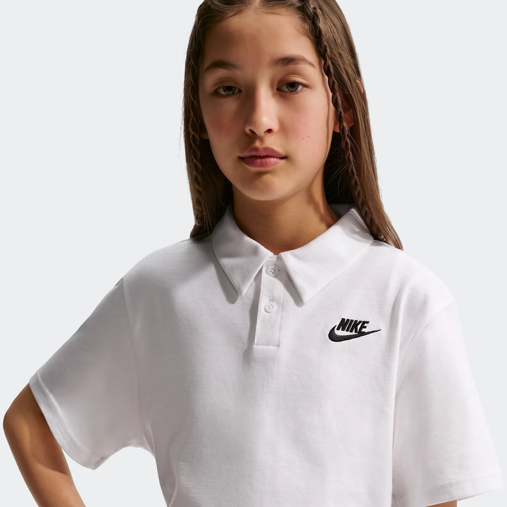 Young girl wearing a white Nike Sportswear Club knit short-sleeve polo shirt with a black swoosh logo.