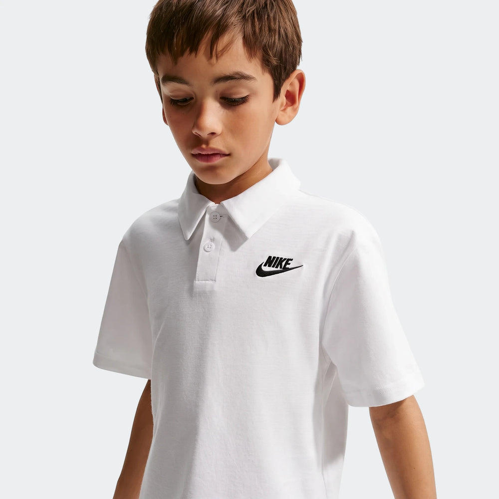Close-up of a boy wearing a white Nike Sportswear Club Big Kids' Knit Short-Sleeve Polo with a black logo on the chest.