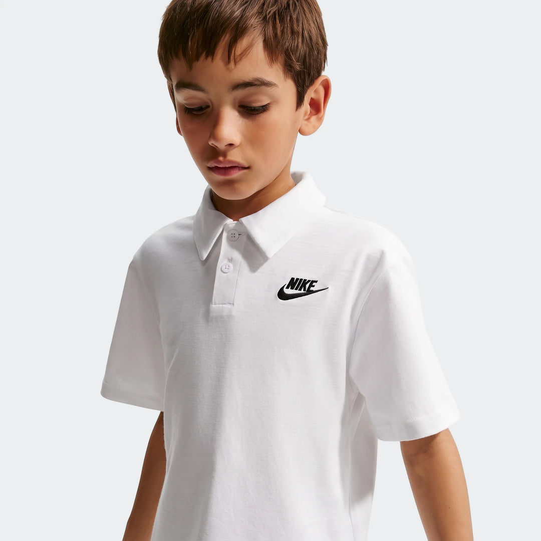 Close-up of a boy wearing a white Nike Sportswear Club Big Kids' Knit Short-Sleeve Polo with a black logo on the chest.