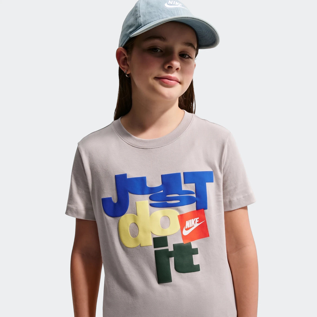 Young girl wears a light gray Nike Sportswear Club T-shirt with multicolored Just Do It graphic and a light blue denim Nike