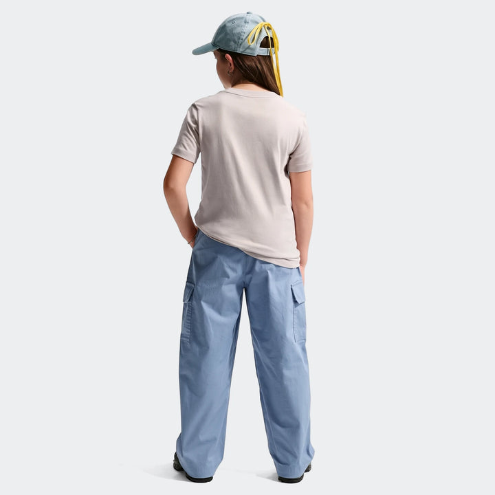 Light gray Nike Sportswear Club Big Kids' T-Shirt, worn by a child from the back, paired with blue cargo pants and a denim