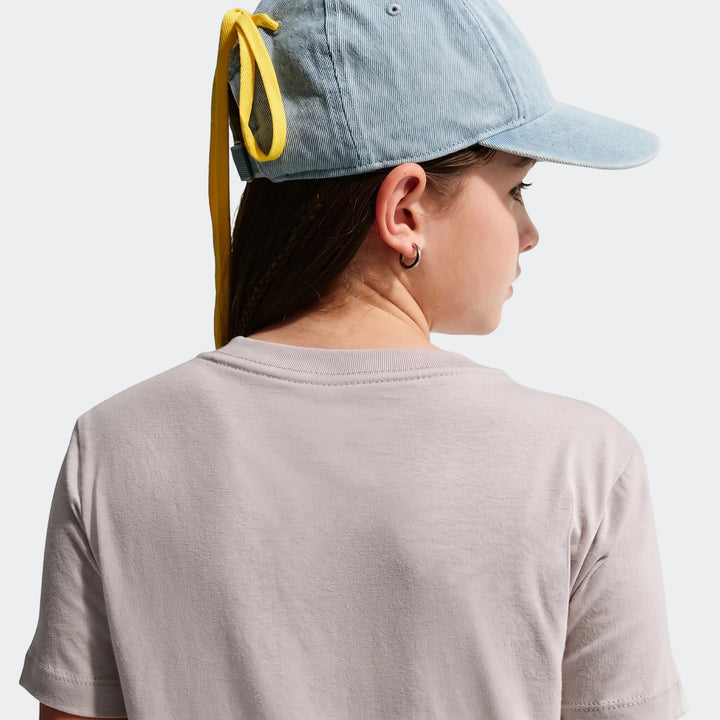 Close-up back view of a young person wearing a light gray Nike Sportswear Club Big Kids' T-Shirt and a light blue denim cap