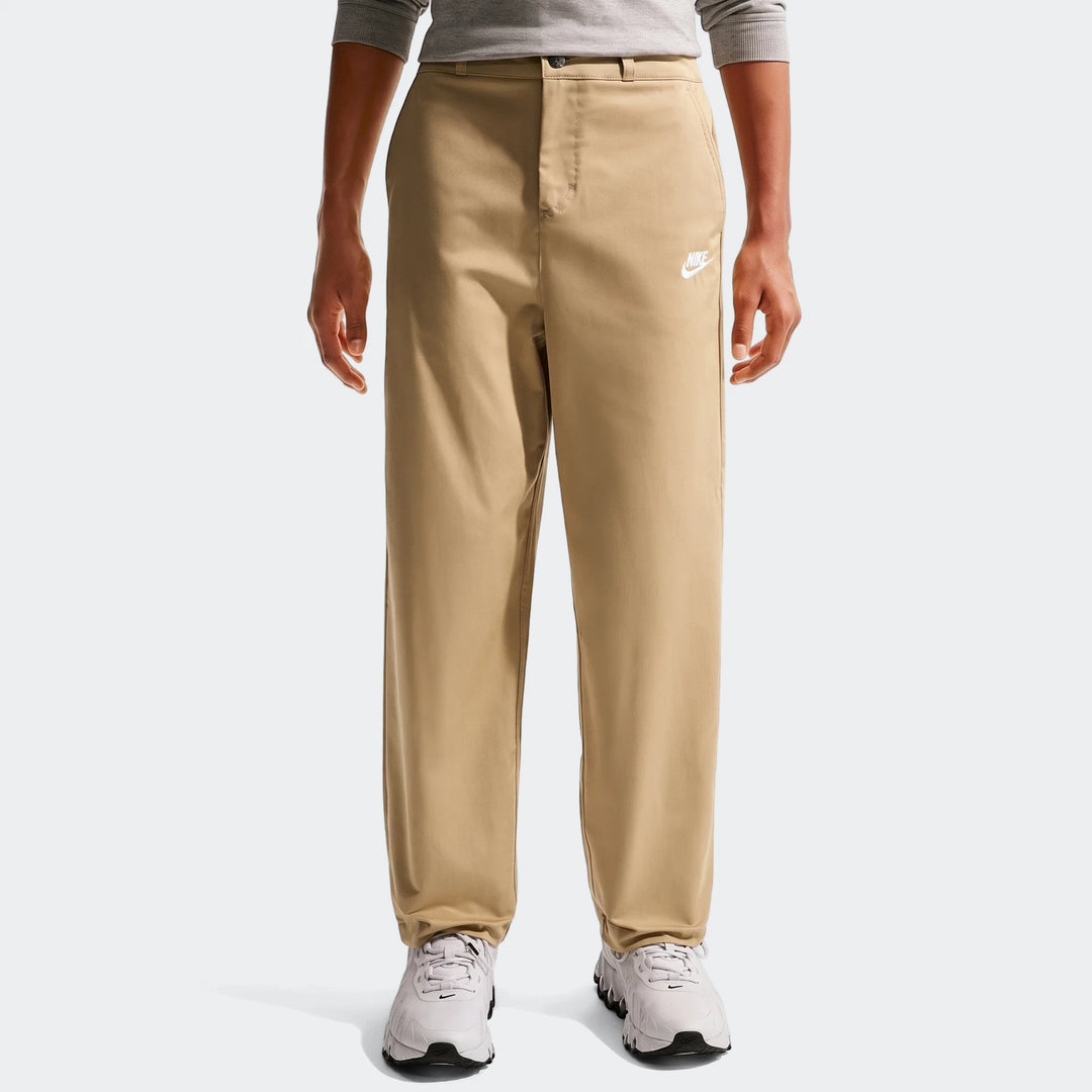 Person wearing Nike Sportswear Club Big Kids' Woven Everyday Pants in khaki with white sneakers, front view.