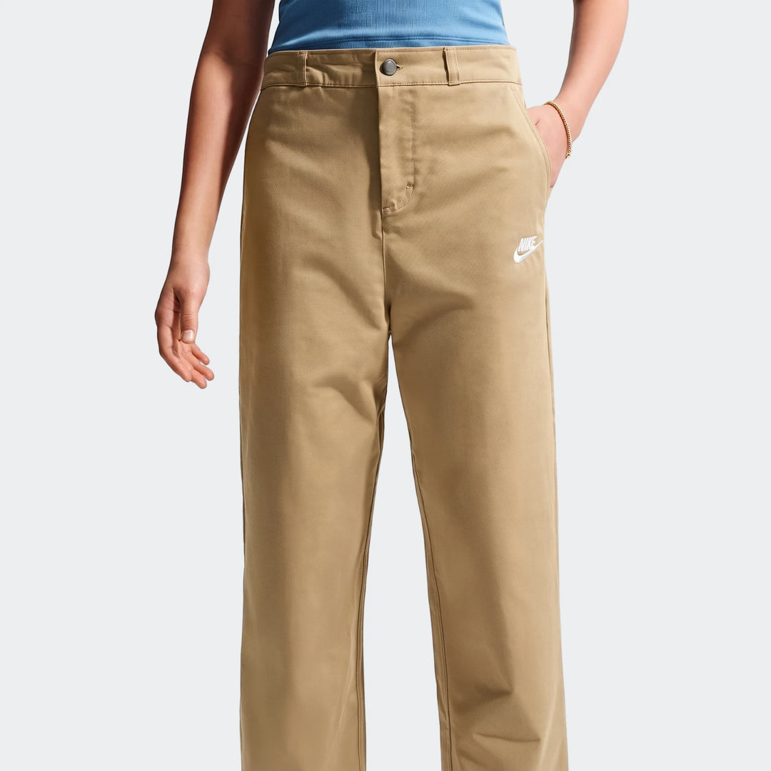 Close-up of a person wearing khaki Nike Sportswear Club Big Kids' Woven Everyday Pants with a white Nike logo.