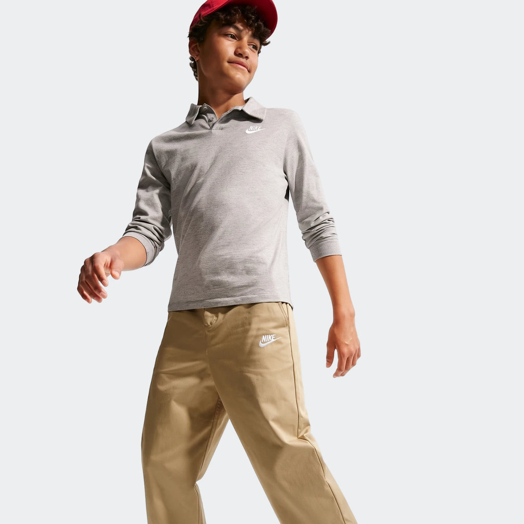 A young boy models khaki Nike Sportswear Club Big Kids' Woven Everyday Pants, paired with a grey long-sleeve polo shirt and
