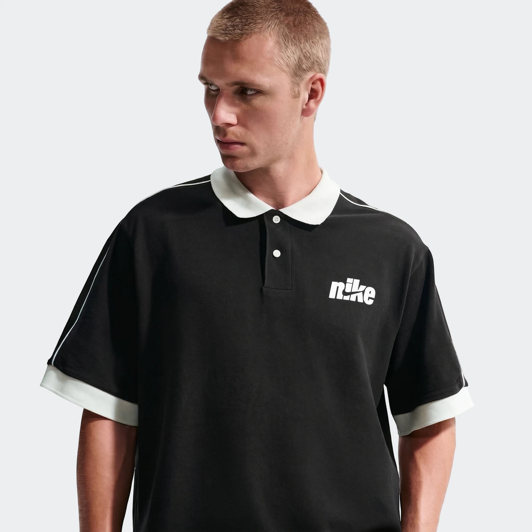 Men's Nike Sportswear Club black oversized short-sleeve polo shirt worn by a model, featuring a white collar and chest logo.