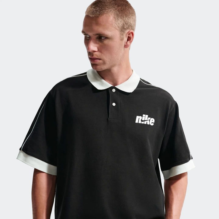 Men's Nike Sportswear Club black oversized short-sleeve polo shirt worn by a model, featuring a white collar and chest logo.
