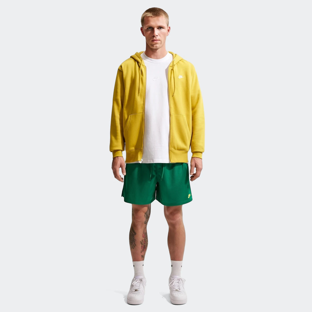 Man wearing Nike Sportswear Club Green Men's Flow Shorts, a yellow hoodie, and a white t-shirt, standing.