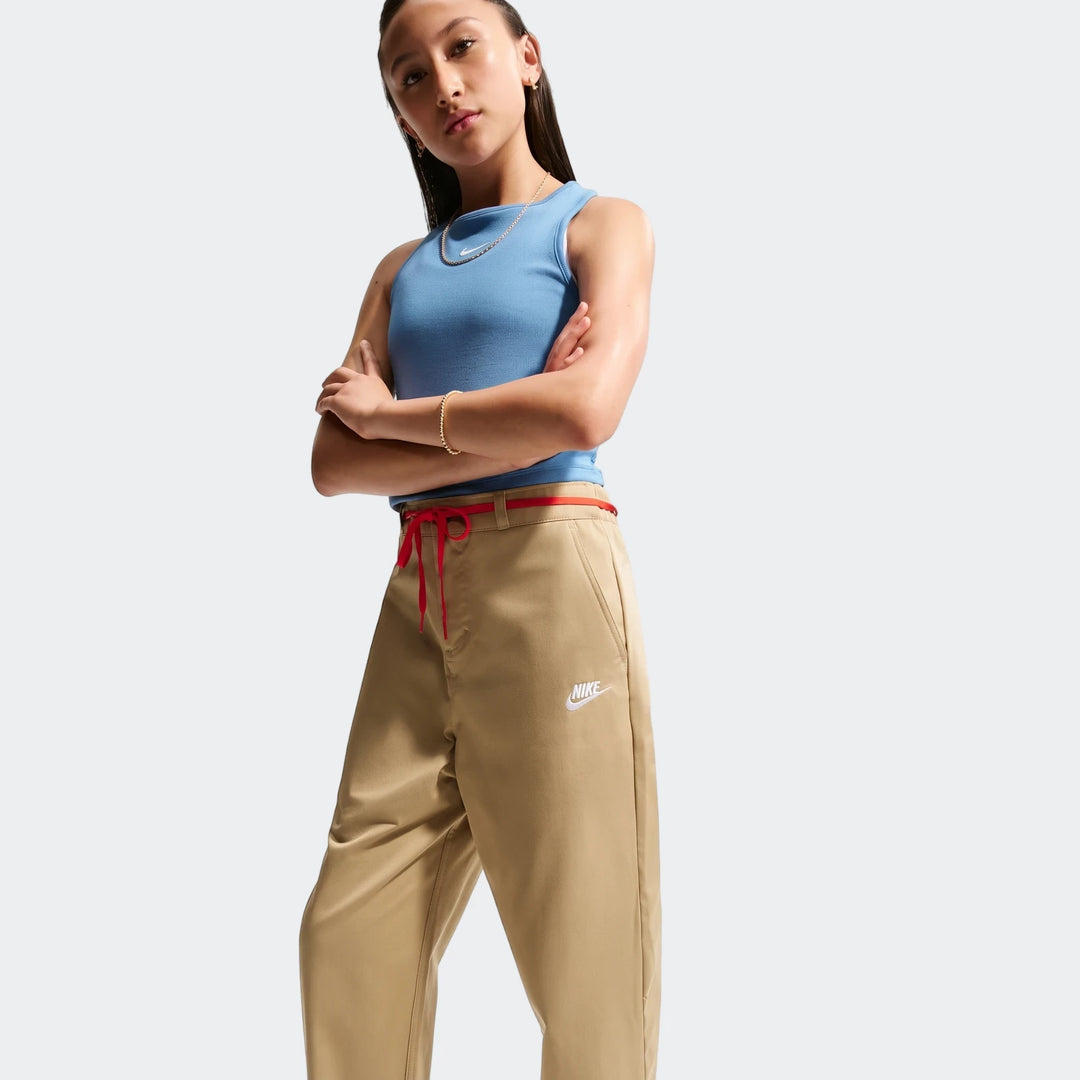 Young person models Nike Sportswear Club Big Kids' Woven Everyday Pants in beige with a red drawstring and embroidered Nike