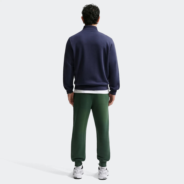 Rear view of a man wearing dark green Nike Sportswear Club Men's Joggers paired with a navy quarter-zip sweatshirt and white